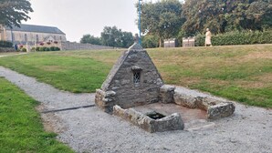 A stone structure with a small window, surrounded by a gravel path and grassy area.