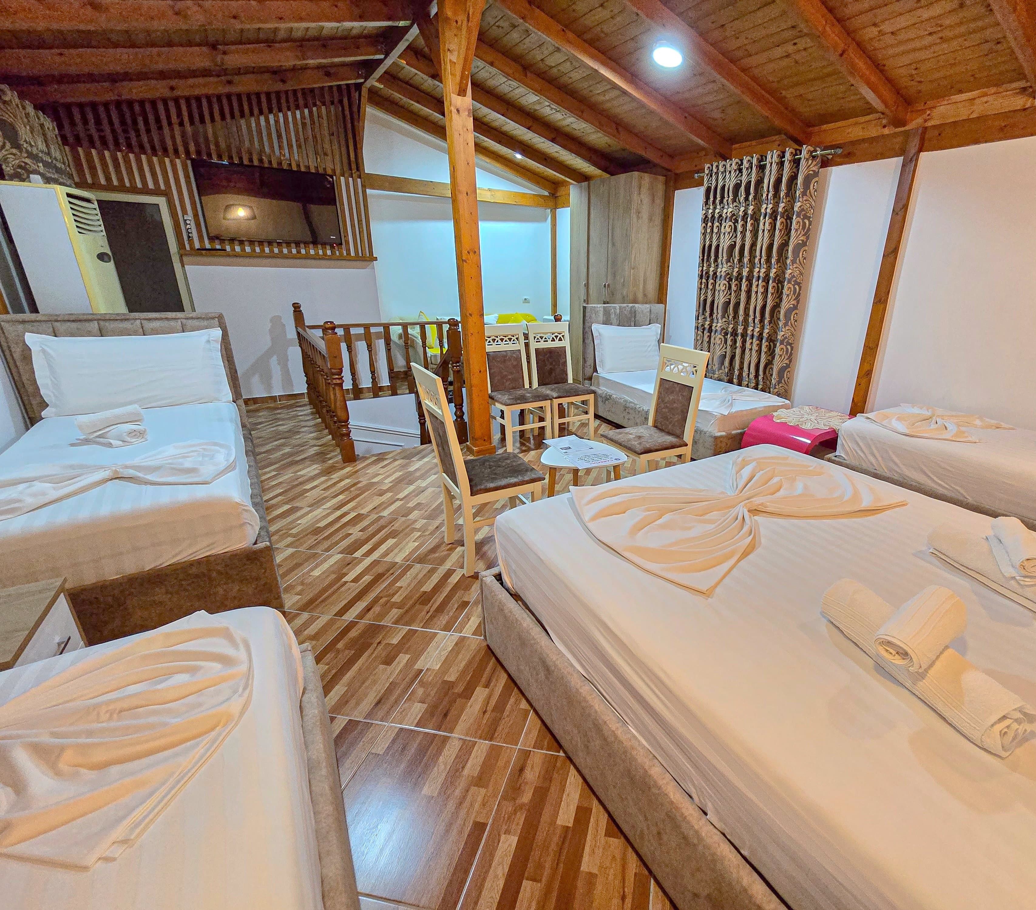 A hotel room with wooden floors, multiple beds, a dining table, chairs, and a balcony.