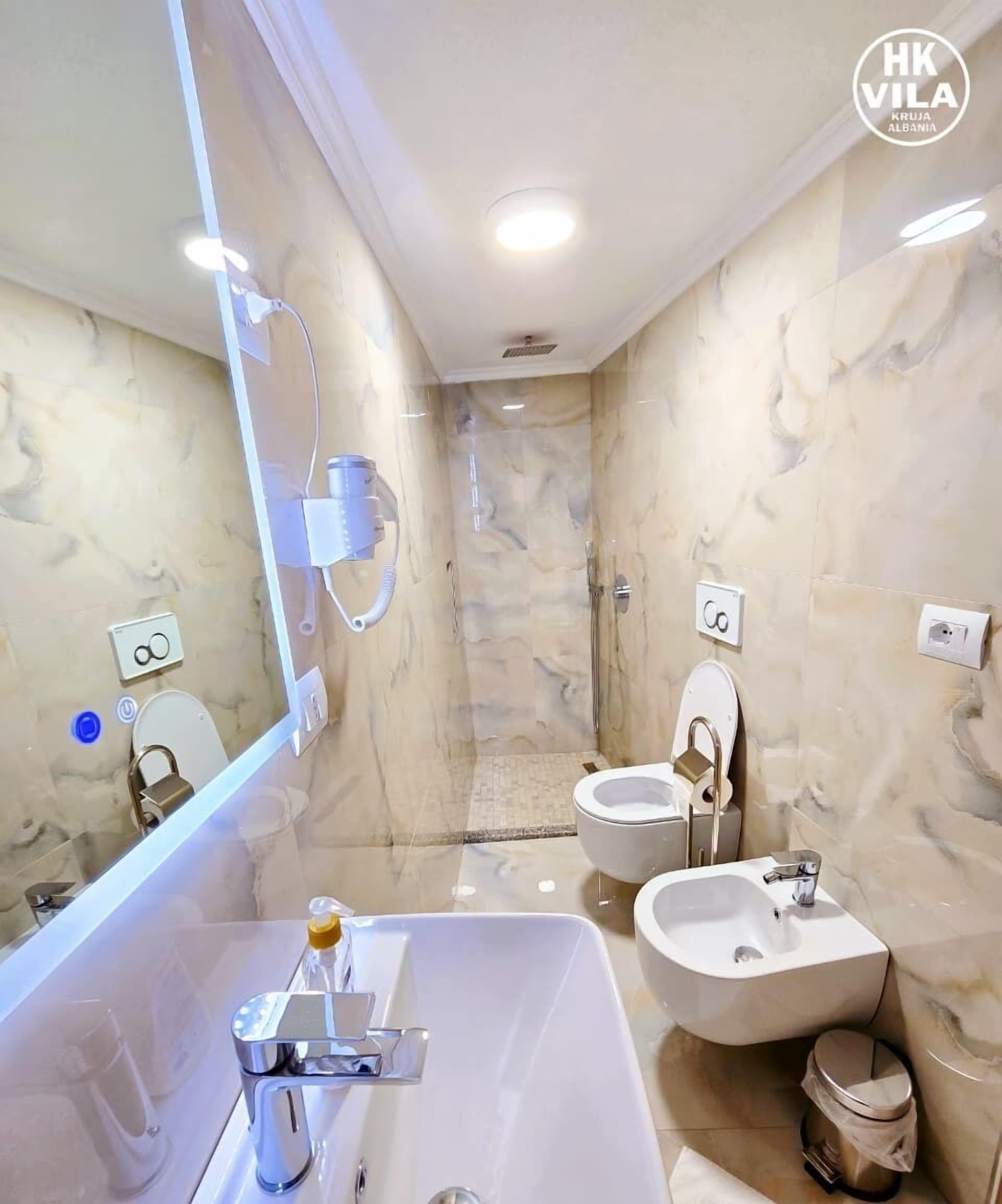 Ein modernes Badezimmer mit großem Spiegel, zwei Waschbecken, einer Dusche und Marmorwänden.