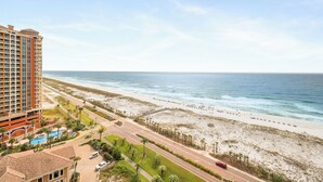 A high-rise hotel with a beach view, a swimming pool, and a road leading to the beach.