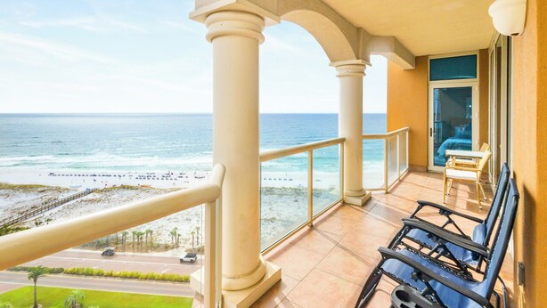 A balcony with a view of the ocean, a beach, and a road.