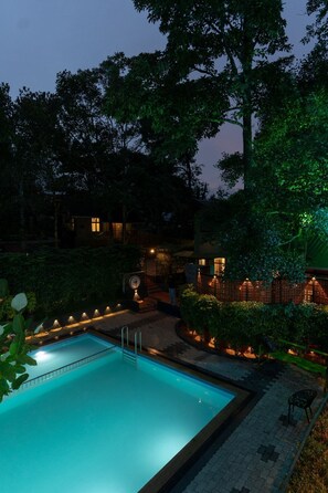A swimming pool surrounded by a landscaped garden with a building in the background. - Swiss Holidays (Vythiri)