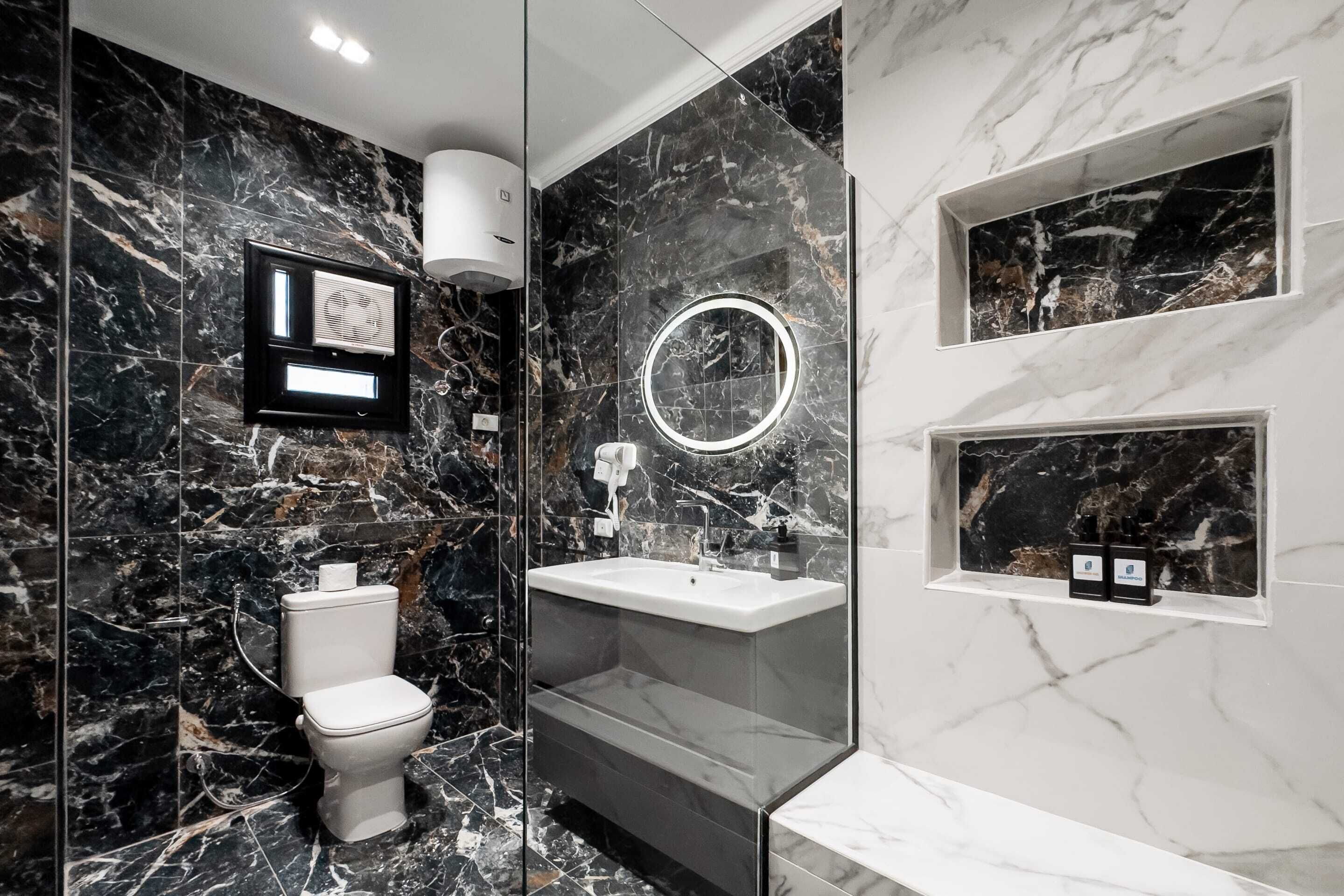 A modern bathroom with a toilet, sink, and mirror, featuring marble walls and built-in shelves.