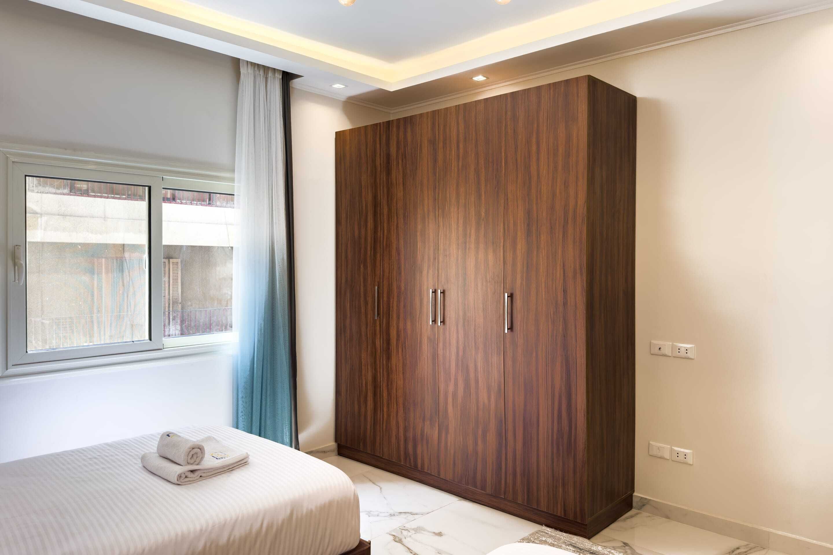 A bedroom with a bed, a wardrobe, and a window with curtains.