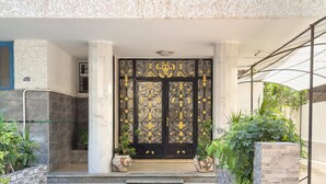 A modern entrance with a decorative black gate, potted plants, and a tiled pathway leading to a building.