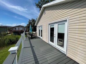 A covered outdoor deck with a table and chairs, a sliding glass door, and a view of neighboring houses.