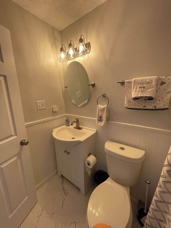 A bathroom with a white sink, mirror, and toilet. There is a towel rack with a towel and a sign that says "Choose to be kind."