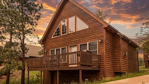 Une cabane en rondins à deux étages, dotée d’un balcon, de grandes fenêtres et d’un garage.
