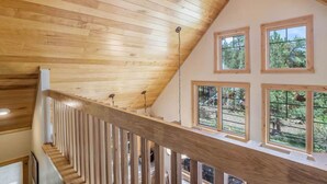 A wooden staircase with a railing leading to a second-floor area with large windows. - Luxe Mountain Cabin! Views, jetted tub, deck, BBQ (Estes Park)