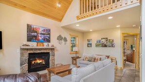 A cozy living room with a stone fireplace, a large sofa, and a television mounted above it. - Luxe Mountain Cabin! Views, jetted tub, deck, BBQ (Estes Park)
