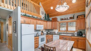 A kitchen with wooden cabinets, a white refrigerator, a microwave, a stove, and a dining table with chairs. - King beds, deck, views, fire place & hot tub (Estes Park)