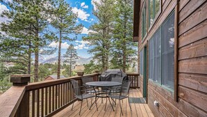 A wooden deck with a table and chairs, overlooking a mountainous landscape. - King beds, deck, views, fire place & hot tub (Estes Park)
