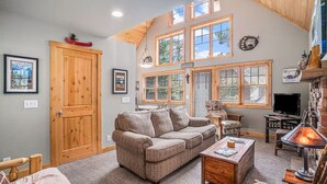 A cozy living room with a wooden ceiling, a large window, a fireplace, and a television. - King beds, deck, views, fire place & hot tub (Estes Park)