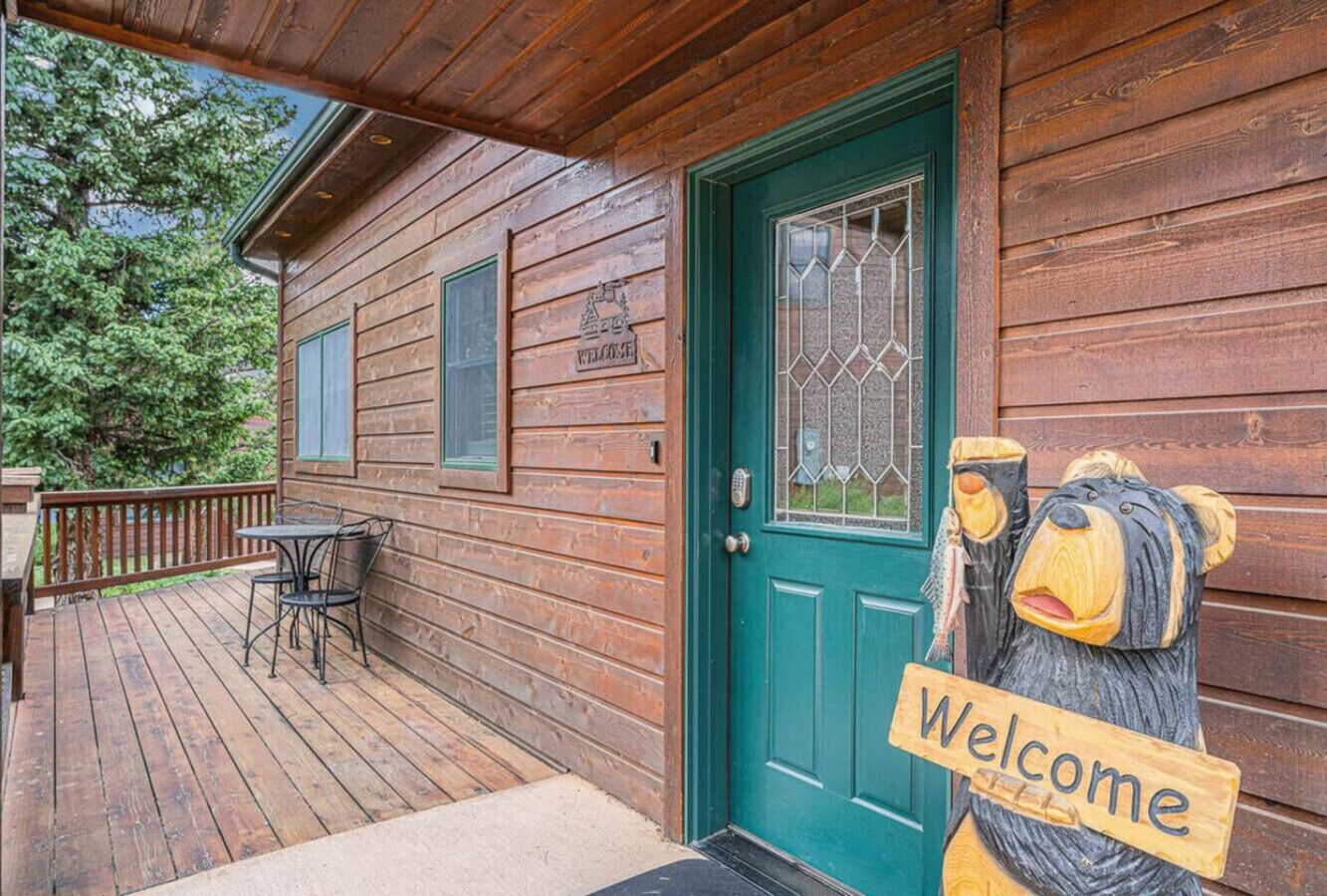 Une cabane en bois avec une porte verte, une pancarte indiquant « Bienvenue » et une petite table et une chaise sur le porche.
