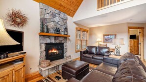 A cozy living room with a stone fireplace, leather sofas, and a television. - Wildlife, shared hot tub, fireplace, deck, BBQ! (Estes Park)