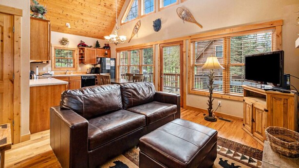 A cozy cabin interior with a leather sofa, wooden dining table, and a kitchen area. - Wildlife, shared hot tub, fireplace, deck, BBQ! (Estes Park)