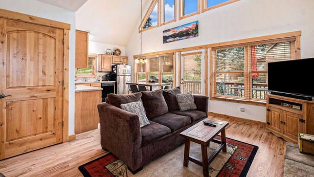 A spacious living area with a high ceiling, wooden flooring, a brown sofa, a coffee table, and a TV stand. - Upstairs AC! Fireplace, deck, BBQ, shared hot tub (Estes Park)