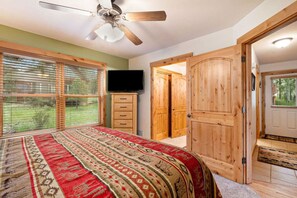 Quarto com cama, ventilador de teto, televisão e portas de madeira.