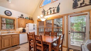 A kitchen with wooden cabinets, a dining table with chairs, a refrigerator, and a window with blinds.