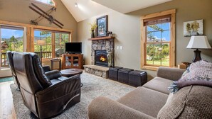 Una sala de estar acogedora con chimenea, sillones de cuero, un sofá y ventanas amplias que ofrecen vistas al exterior.