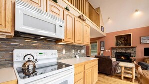 A modern kitchen with wooden cabinets, a white stove, and a stone fireplace. - Panoramic RMNP Views. K beds, deck, fireplace, BBQ (Estes Park)