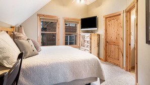 A bedroom with a bed, a ceiling fan, a TV, wooden doors, and a window. - Epic views, BBQ, deck, fireplace, shared hot tub! (Estes Park)