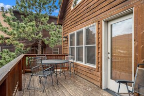 A wooden deck with a table and chairs, a door, and a view of a pine tree. - Cabin, views, K bed, shared hot tub, BBQ, deck! (Estes Park)