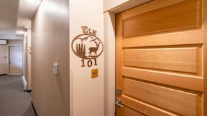 Un couloir avec une porte en bois portant le numéro « 101 » et un motif décoratif mural représentant un cerf et des arbres.