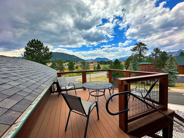 A wooden deck with a metal railing, a round table, and two chairs.
