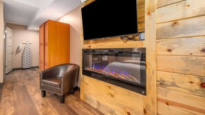 A room with a fireplace, a leather chair, and a TV mounted on a wooden wall. - ADA King Room, AC, Fireplace, hot tub - Lodge 103 (Estes Park)