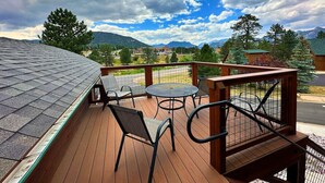 A wooden deck with a metal railing, a round table, and two chairs. - ADA King Room, AC, Fireplace, hot tub - Lodge 103 (Estes Park)