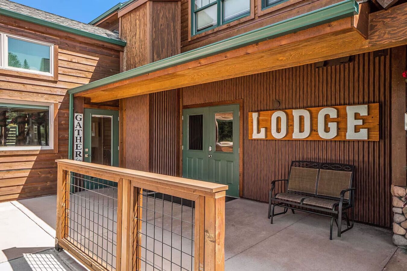 Una cabaña de madera con puerta verde, un letrero que dice 'Lodge' y un banco en el exterior.