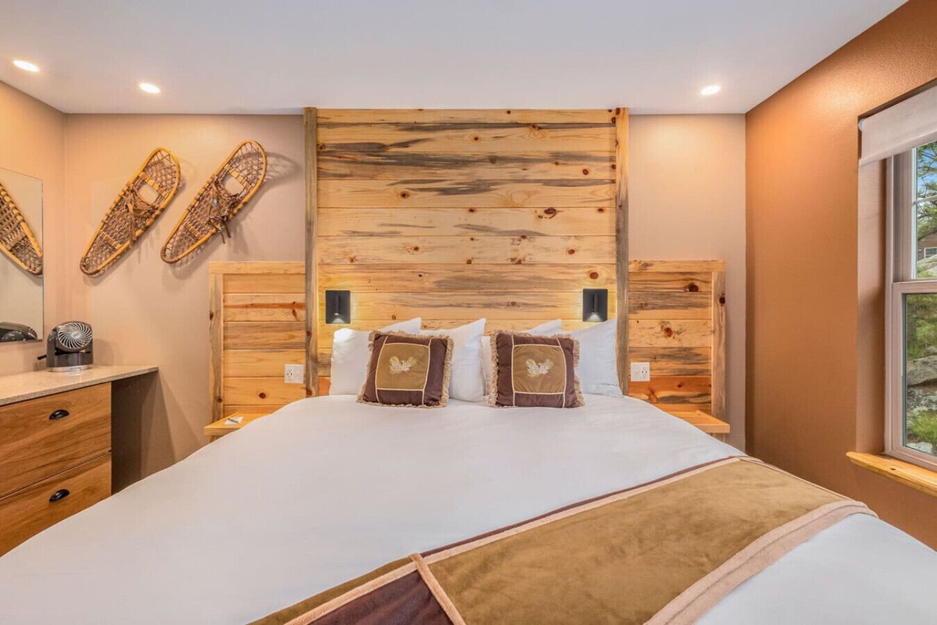 Ein Schlafzimmer mit einem großen Bett, einem Holzkopfteil, zwei Nachttischen, einem Schminktisch und einem Fenster mit Blick.