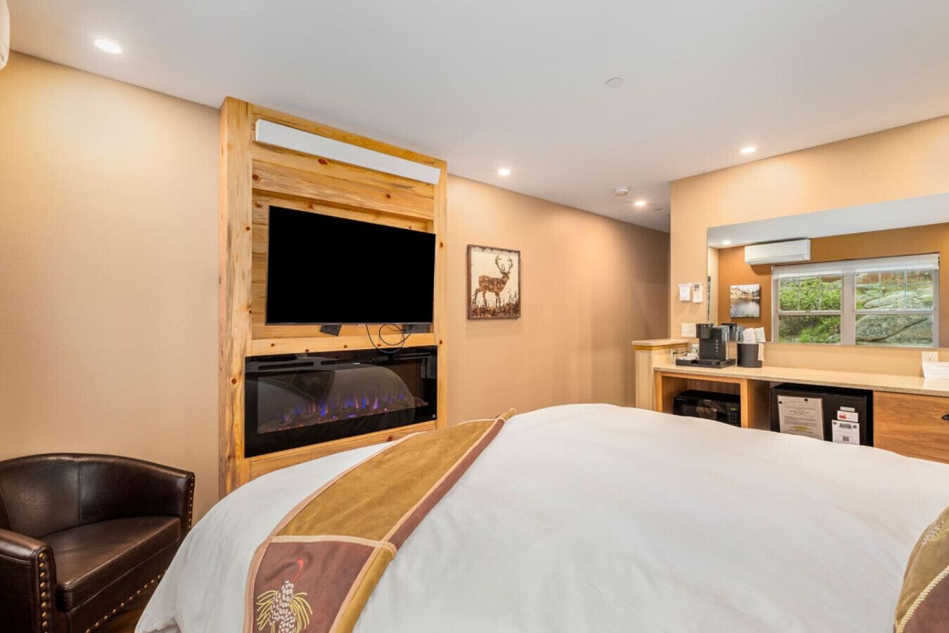 Une chambre d’hôtel équipée d’un lit, d’une cheminée, d’une télévision, d’un bureau avec un ordinateur et d’une fenêtre donnant sur un paysage verdoyant.