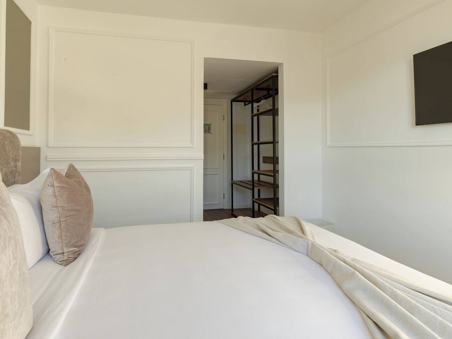 A hotel room with a bed, pillows, a wardrobe, and a television on the wall.