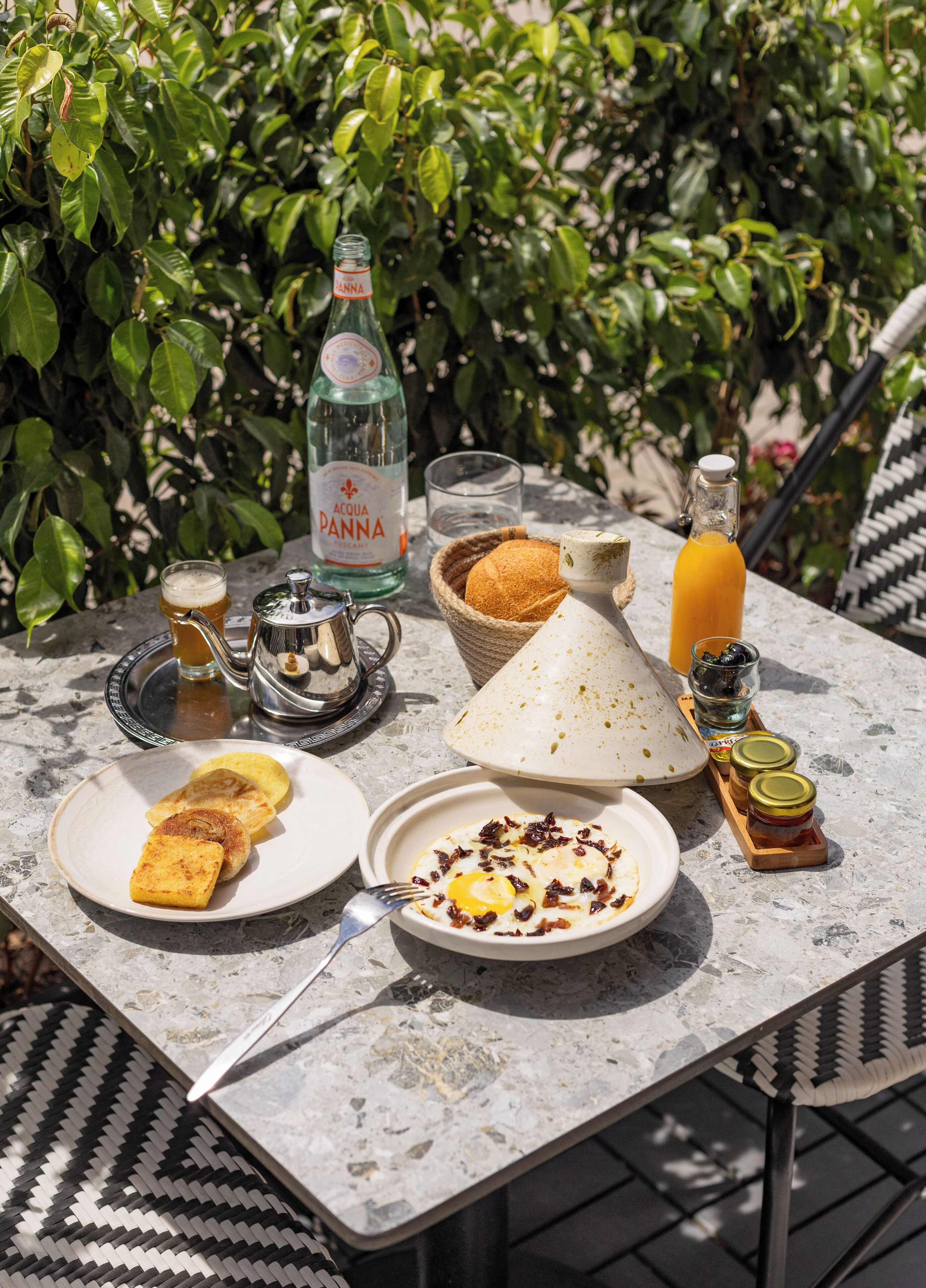 A table set with breakfast items including toast, eggs, and condiments, with a bottle of Acqua Panna water and a basket of bread.