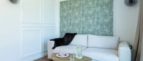 A modern living room with a white sofa, a round wooden coffee table, and a decorative wall panel.