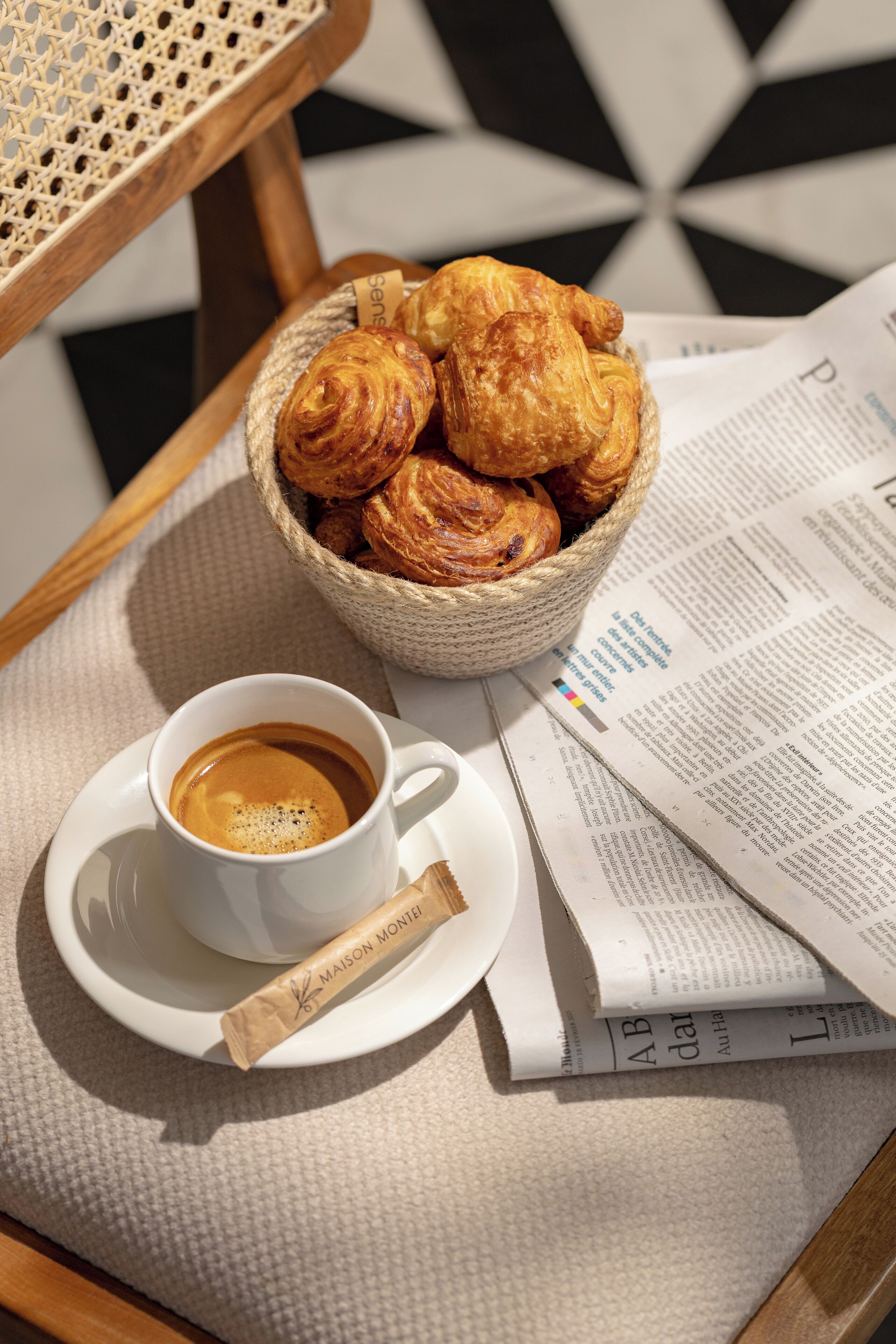 Una cesta de cruasanes, una taza de café y un periódico sobre una mesa.