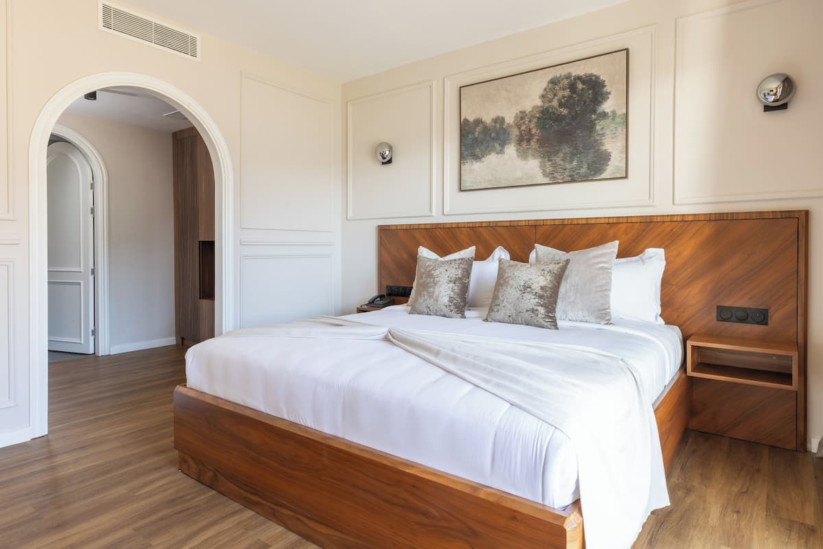 Un dormitorio con una cama de madera, ropa de cama blanca, un cuadro en la pared y una mesita de noche pequeña.