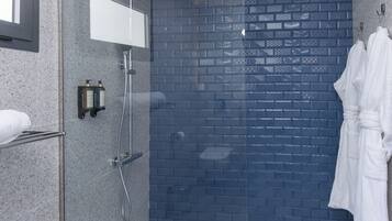 Un área de ducha moderna con puerta de cristal, pared de ladrillo azul y una bata blanca colgada en la pared.