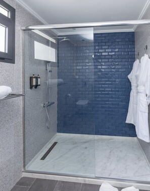 A modern shower area with a glass door, a blue brick wall, and a white robe hanging on the wall. - Aurea Hotel (Tetouan)