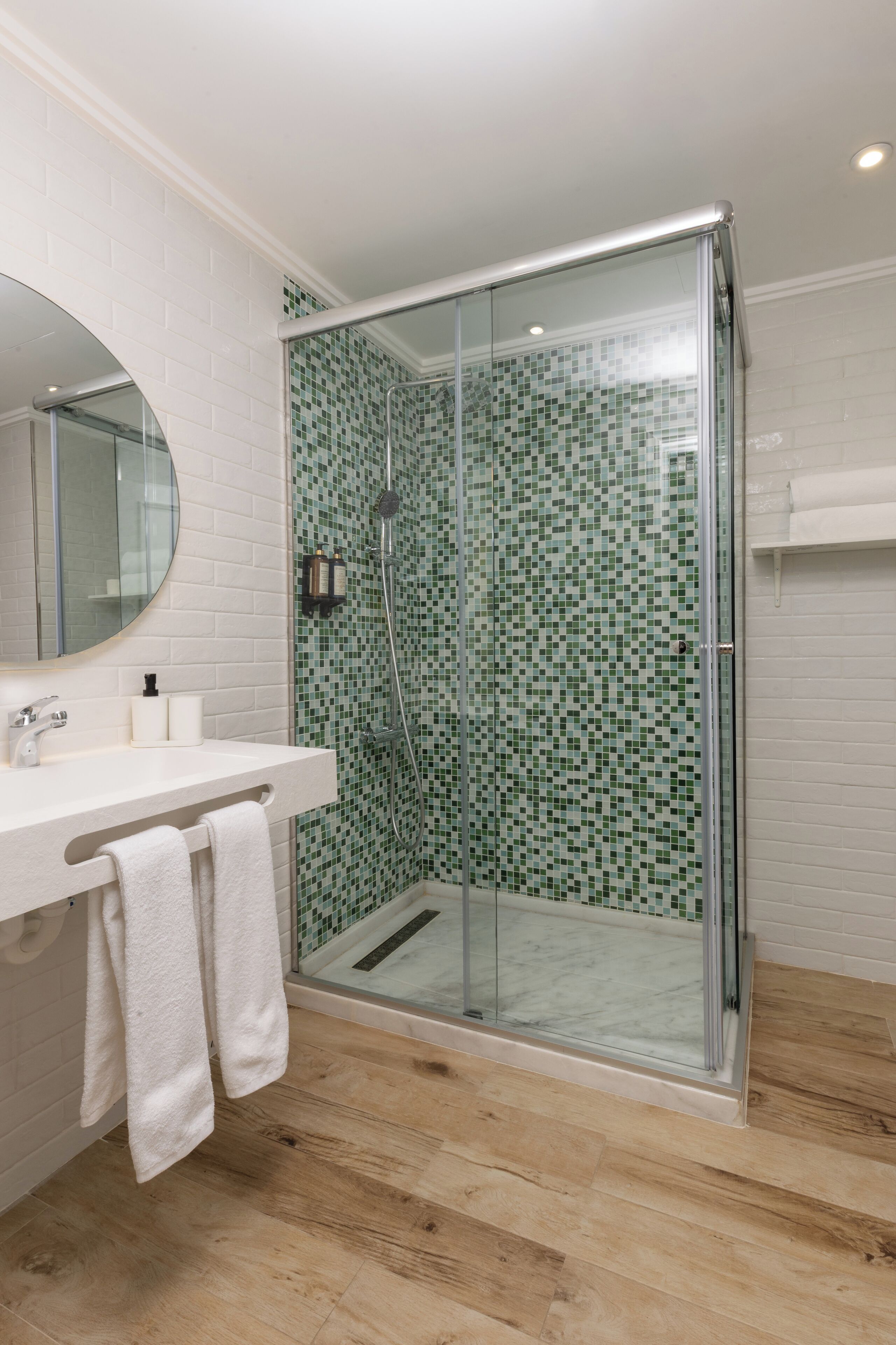 Un baño moderno con ducha de vidrio, paredes de azulejos blancos y suelo de madera.