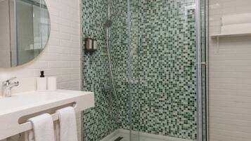 Un baño moderno con ducha de vidrio, paredes de azulejos blancos y suelo de madera.