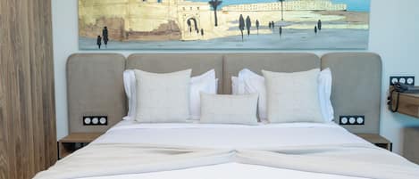 Quarto de hotel com uma cama grande, duas mesas de cabeceira e um quadro de um edifício histórico na parede.