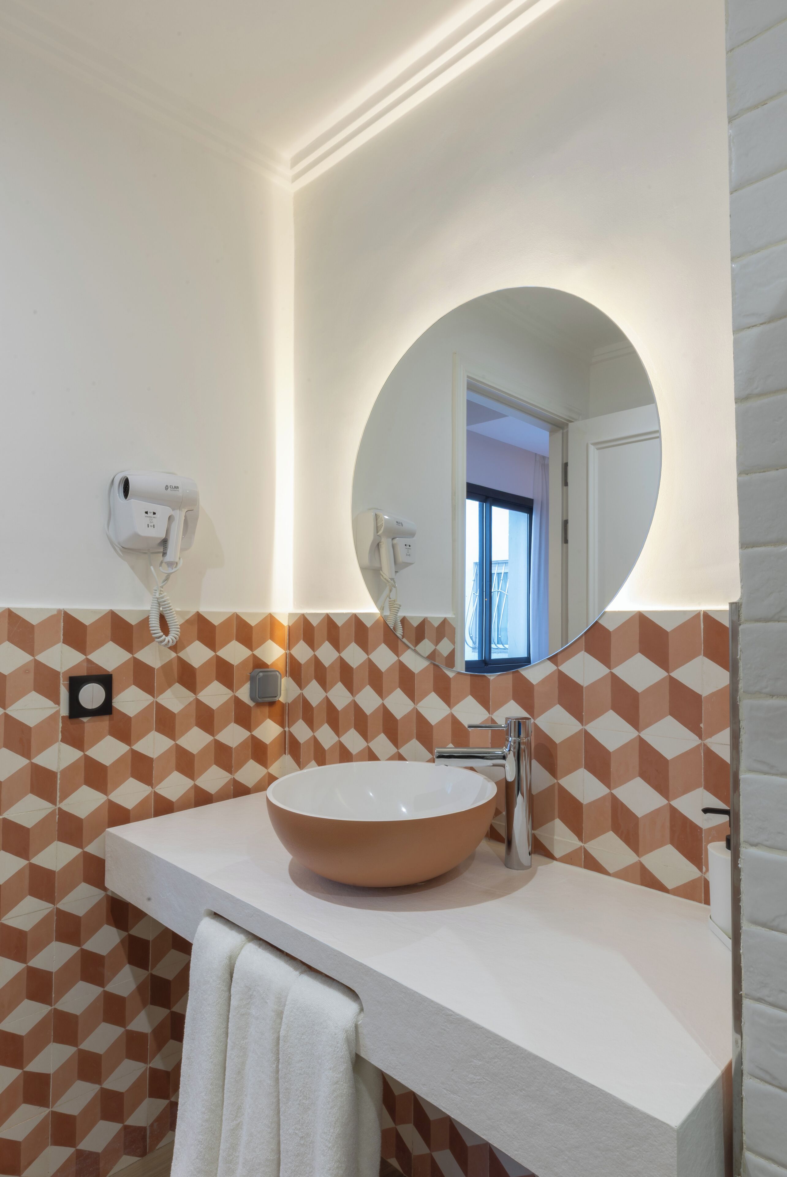A bathroom with a round mirror, a white sink, and a hairdryer mounted on the wall.