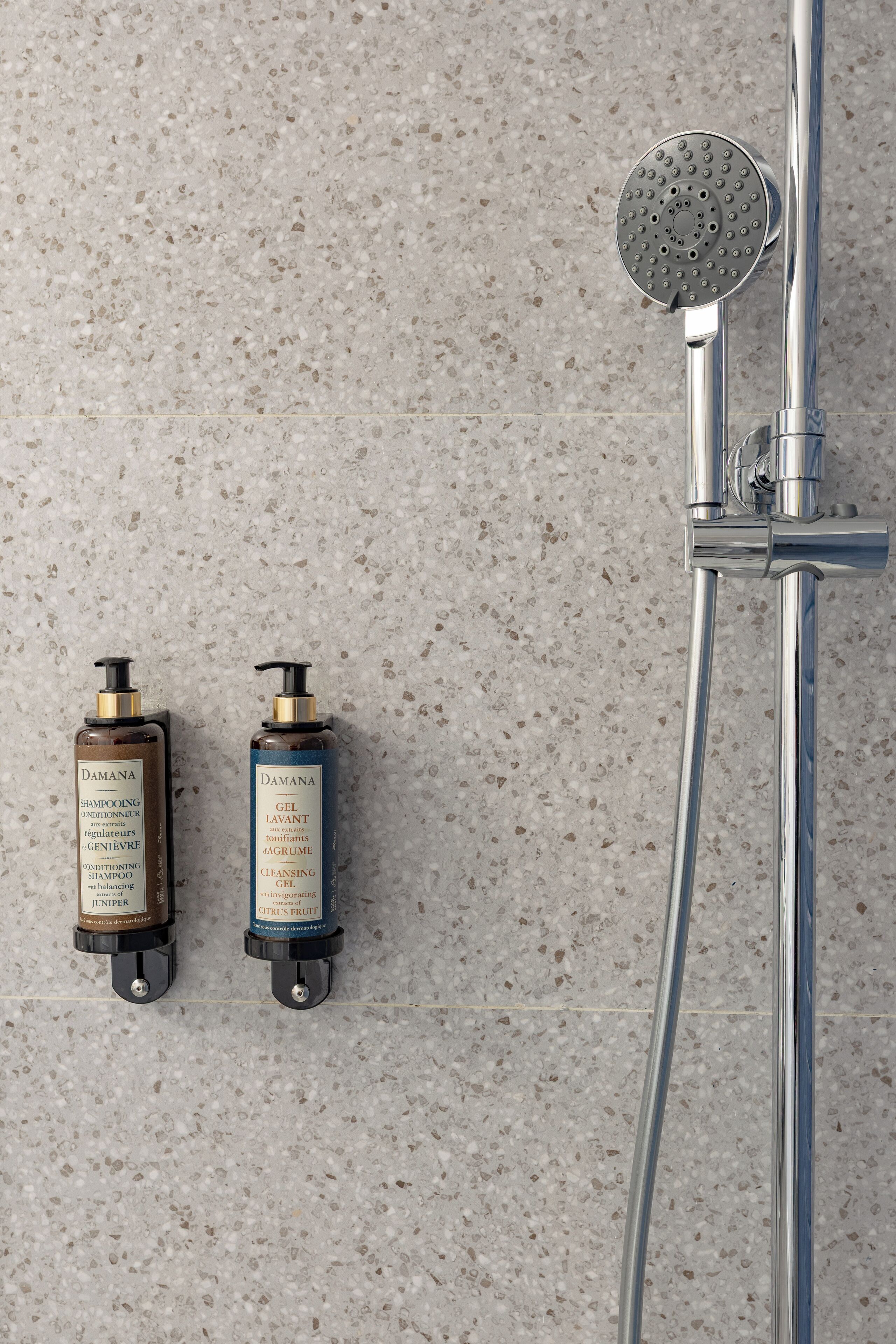 Baño con ducha, dos botellas de champú y pared de azulejos.