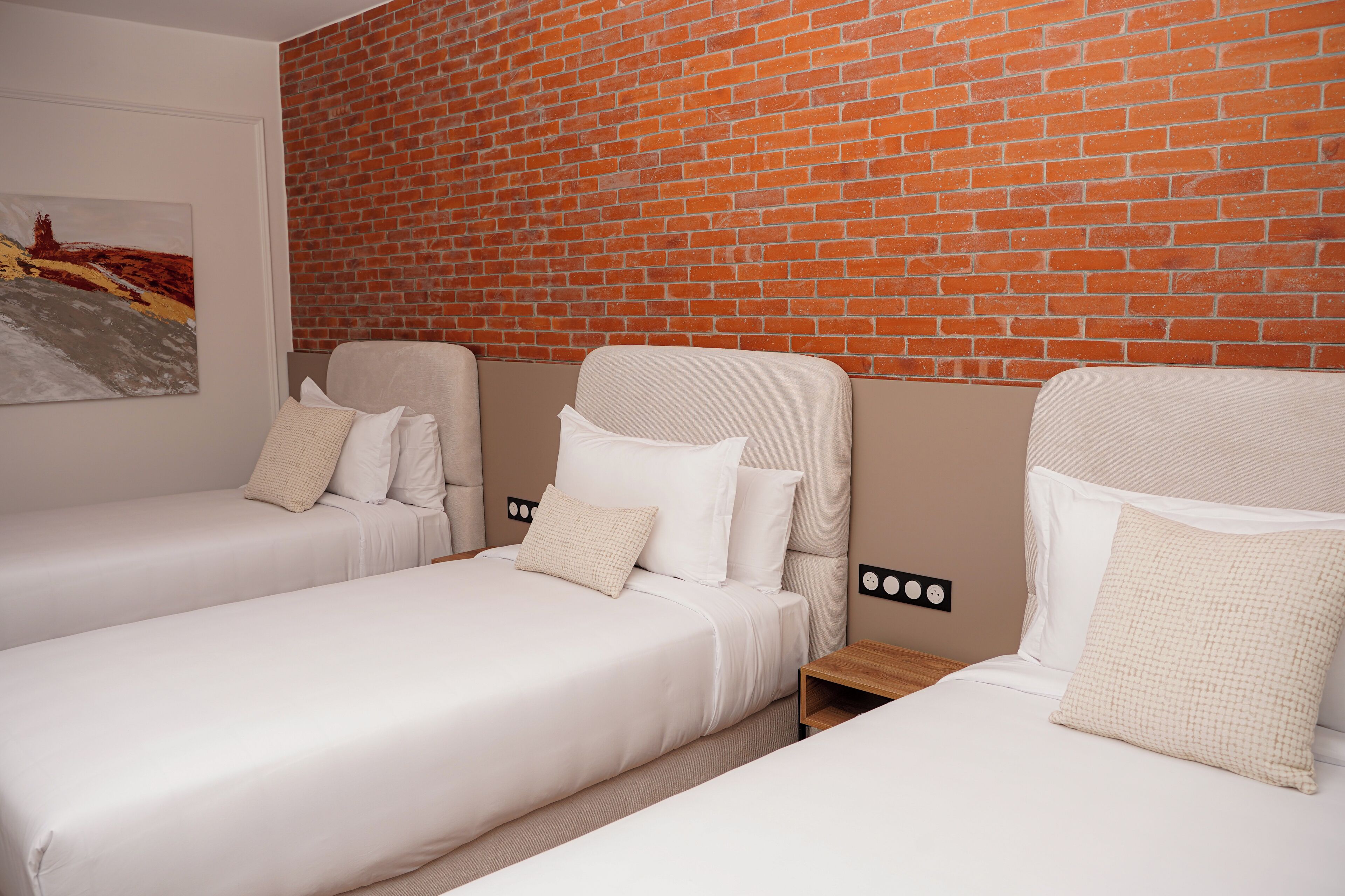 Une chambre d’hôtel avec deux lits simples, un mur en briques et un tableau accroché au mur.