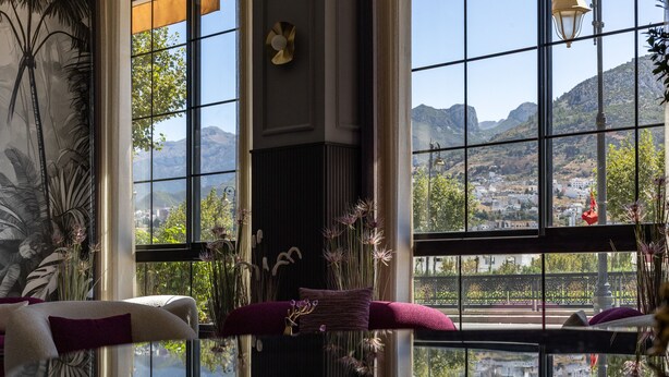 A room with a large window offering a mountain view, a sofa with cushions, and a vase with flowers. - Aurea Hotel (Tetouan)