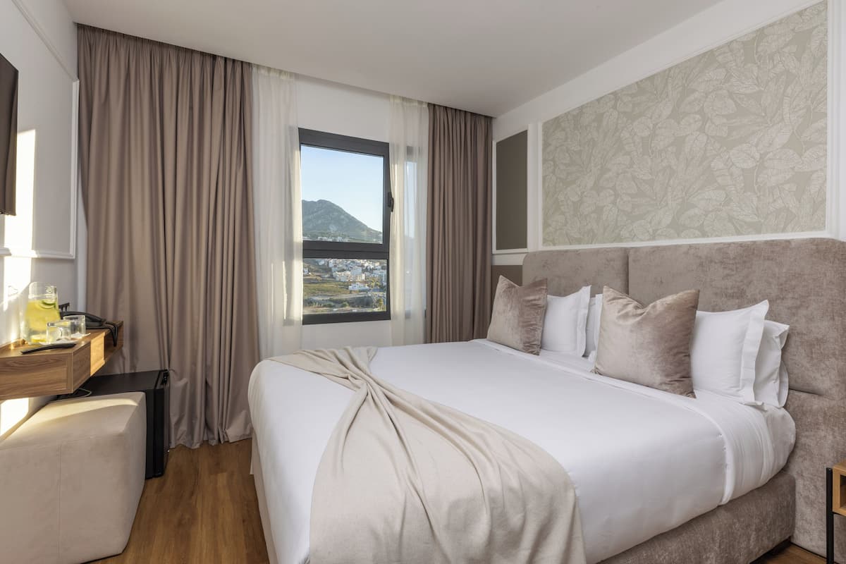 Una habitación de hotel con una cama grande, un escritorio con lámpara y una ventana con cortinas.