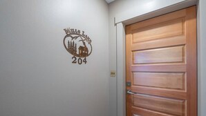 A hotel room with a wooden door, a wall-mounted number plate, and a logo on the wall.